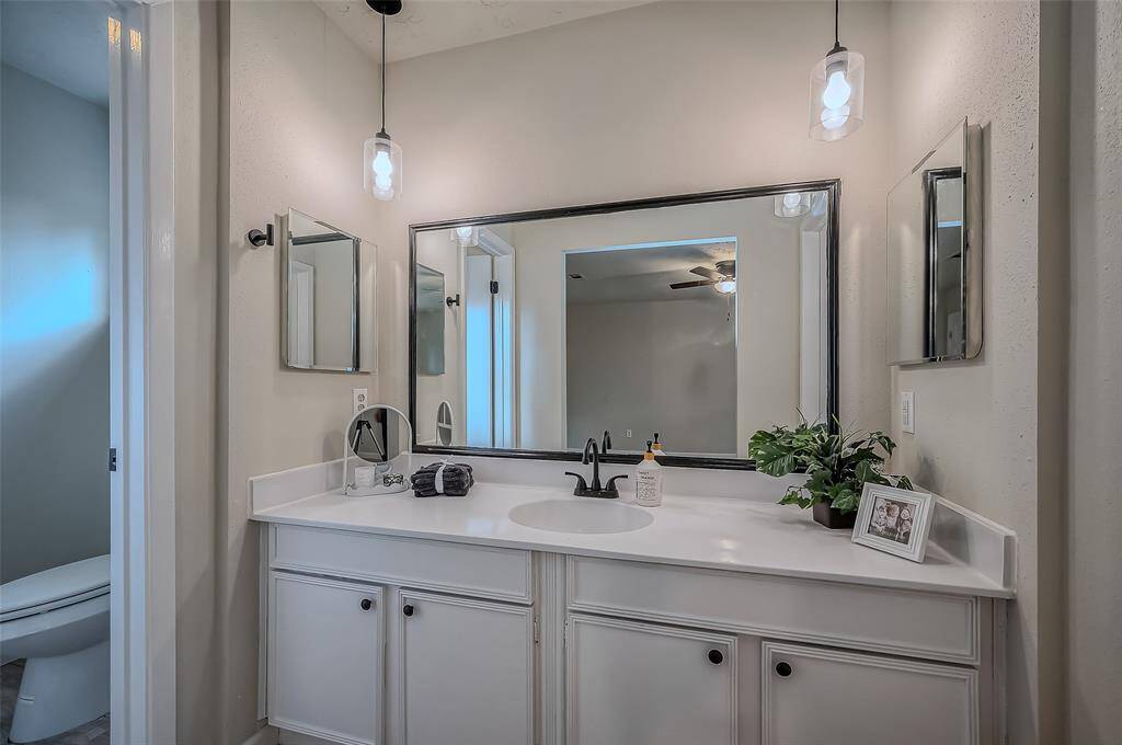 This is a neatly presented bathroom with a large vanity containing ample storage, medicine cabinet and a well-lit mirror. The space is accented with modern pendant lighting and has a clean, neutral color scheme.