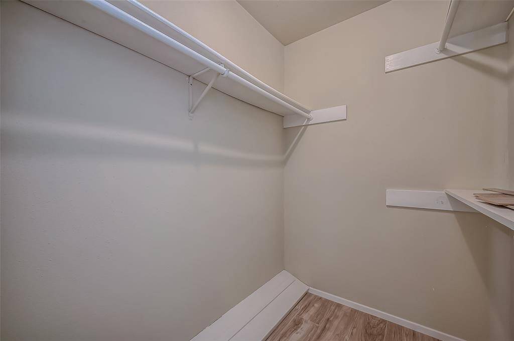Primary walk-in closet featuring multiple shelves and hanging rods, neutral walls and wood-like flooring.