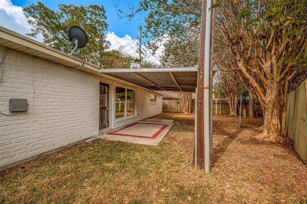 This is an exterior view of a single-story home featuring a cozy covered patio & fenced backyard with mature trees.