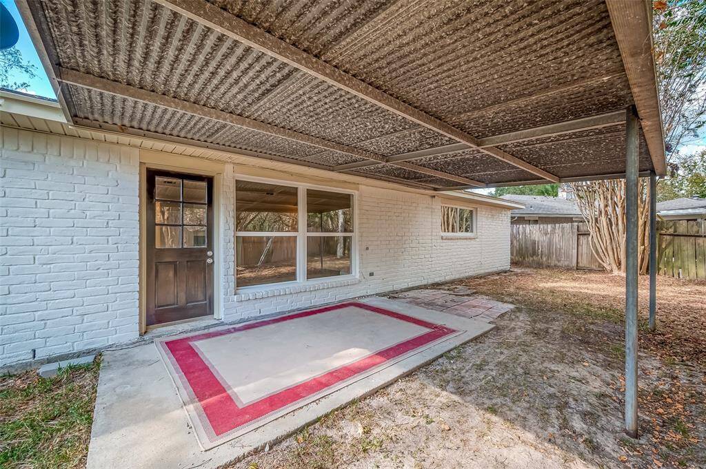 This is a back patio area featuring a covered porch and new large windows on a white-painted brick wall. The yard is fenced, offering privacy.