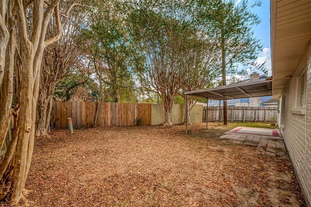Another view of the spacious backyard with mature trees and privacy fence, ready for your outdoor activities.