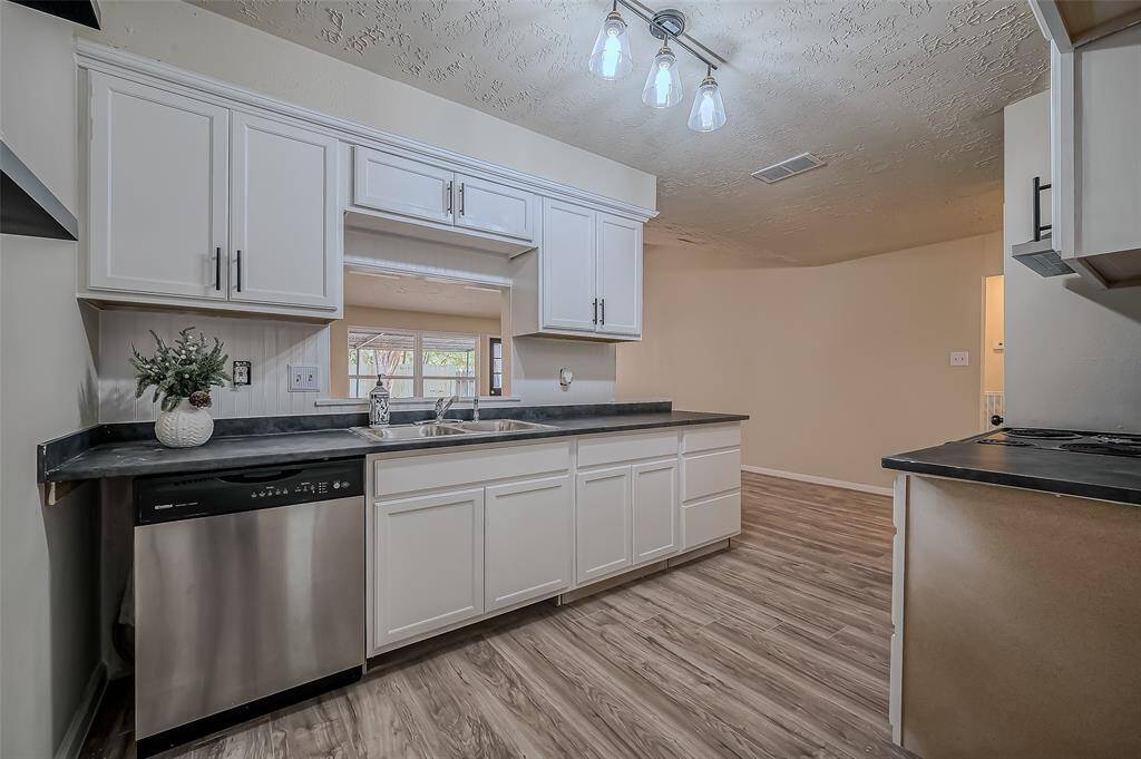 This is a spacious kitchen with modern white cabinetry, stainless steel dishwasher, dark countertops, and a textured ceiling.