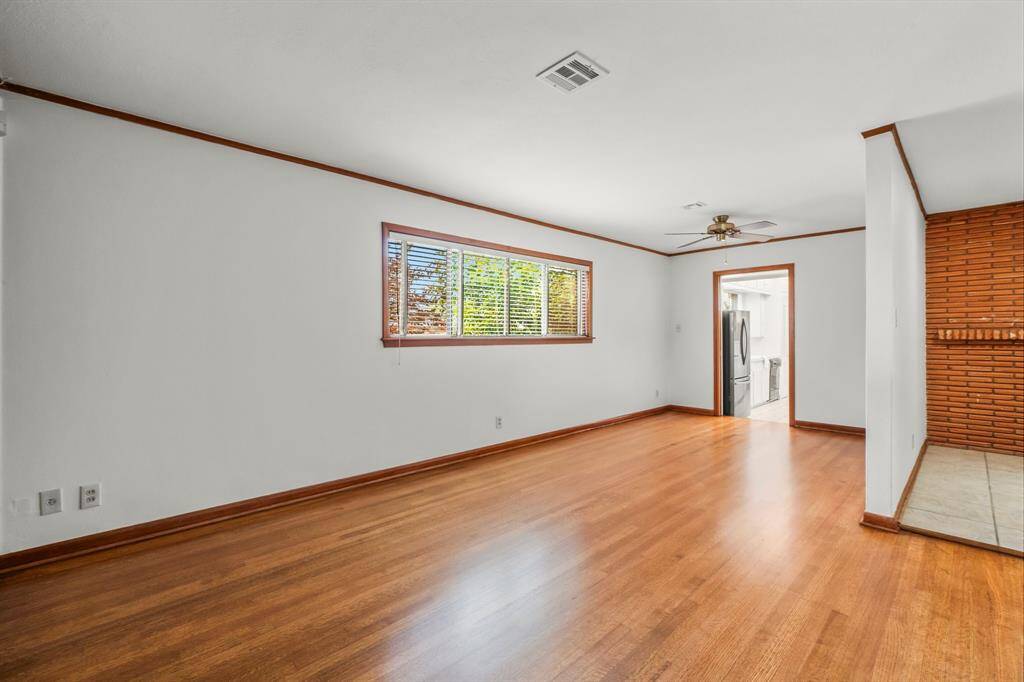 The large Living Room continues toward the kitchen. Notice the fresh paint, beautiful hardwood floors, and ceiling fan!
