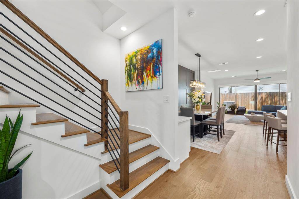 This open-concept living space flows effortlessly from the entry staircase into the dining and living areas, featuring modern lighting fixtures and warm wood tones throughout. The vibrant artwork and thoughtful design create a harmonious balance of comfort and style, ideal for entertaining or family gatherings.