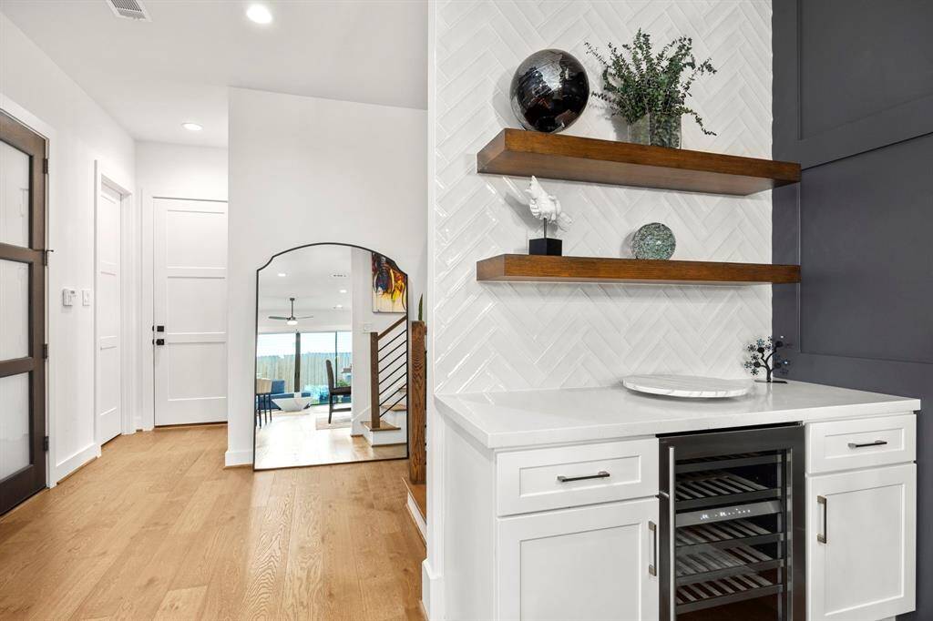 This stylish wet bar area is the perfect blend of modern design and functionality, featuring a herringbone tile backsplash, sleek floating wooden shelves, and a built-in wine cooler. The crisp white cabinetry provides ample storage while complementing the home's contemporary aesthetic, making it an ideal spot for entertaining.