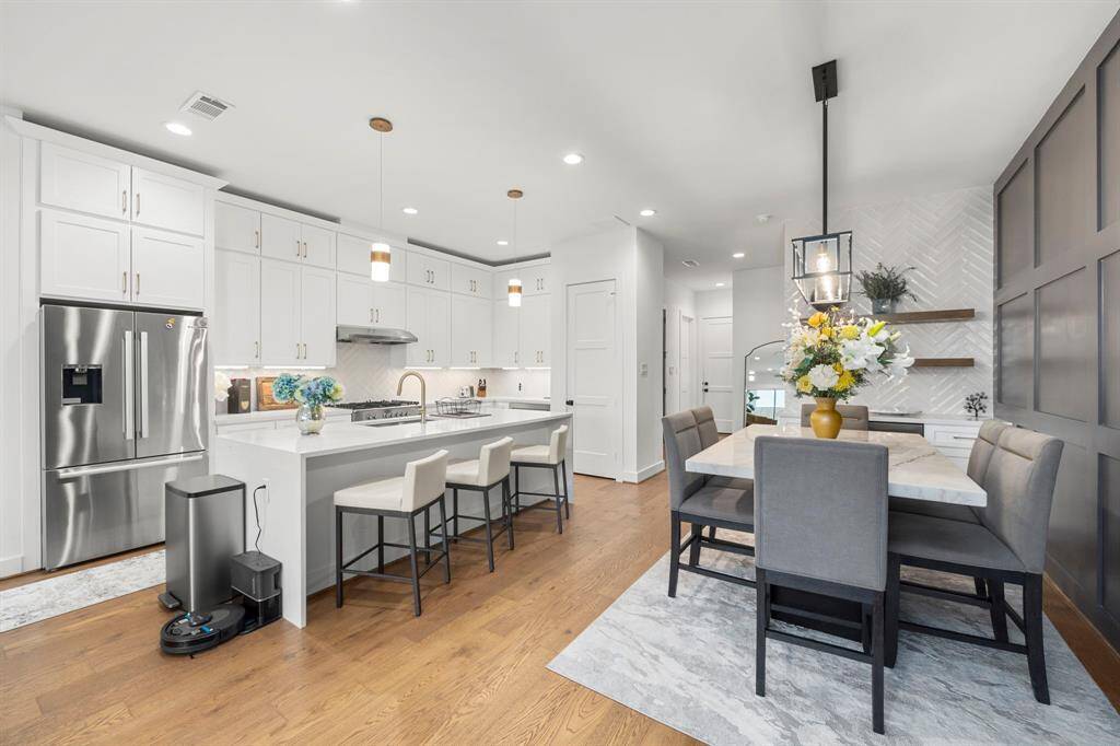 This bright and airy kitchen and dining space offers a perfect blend of functionality and style. The oversized island with seating for three is ideal for casual meals or meal prep, while the adjacent dining area is anchored by a modern chandelier and features a chic accent wall and custom shelving. The combination of sleek appliances and designer finishes elevates the heart of this home, making it perfect for both everyday living and entertaining.