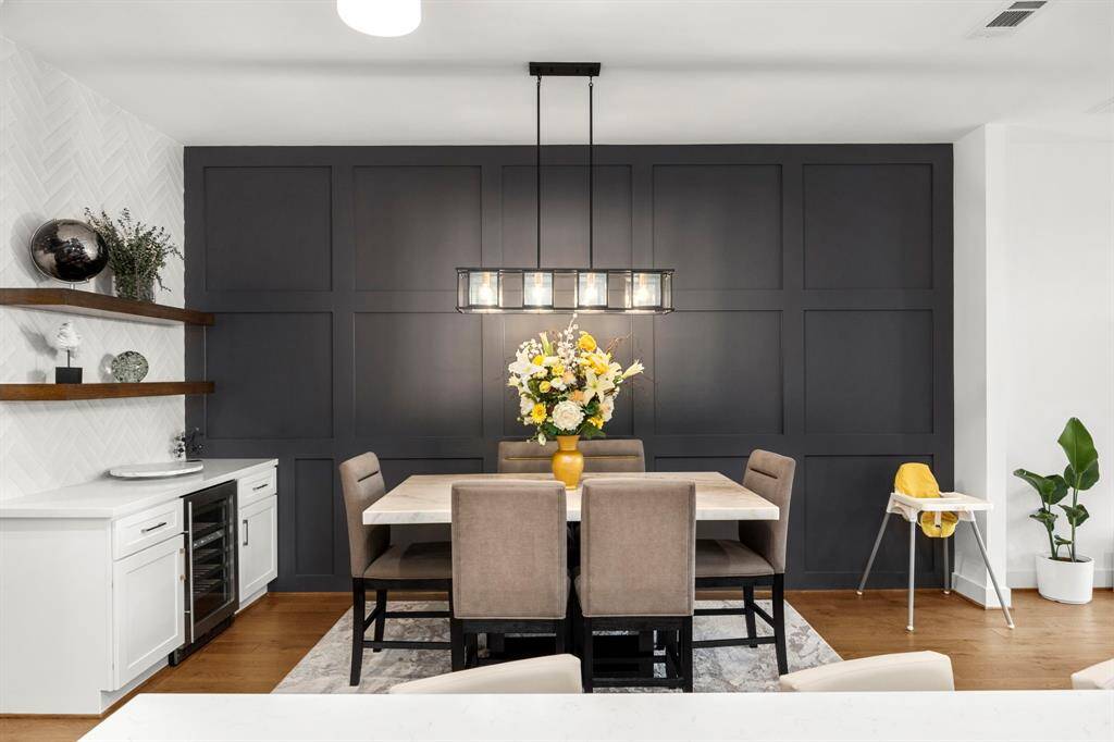 This elegant dining room features a striking accent wall with sophisticated paneling that adds depth and texture to the space. A modern chandelier illuminates the marble-topped dining table, creating a perfect setting for both intimate dinners and larger gatherings. The built-in bar area with floating shelves and a wine cooler provides additional storage and style.