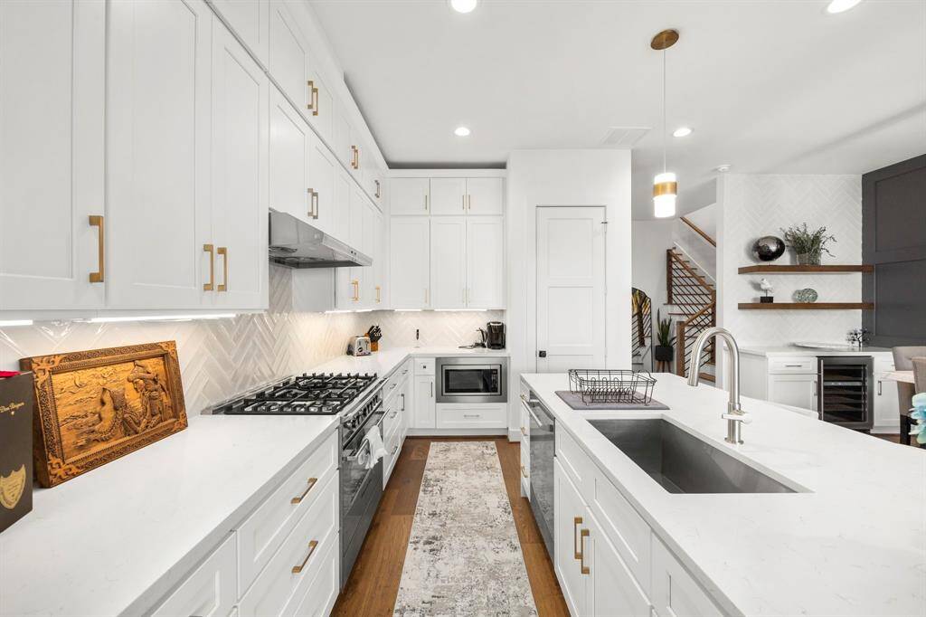 This view highlights the kitchen's abundant storage, with custom cabinetry extending to the ceiling, offering both functionality and style. The gourmet gas range is paired with a modern vent hood and a sleek herringbone tile backsplash. The expansive countertops and built-in microwave create an efficient workspace, while gold hardware adds a luxurious touch to the bright, contemporary design.