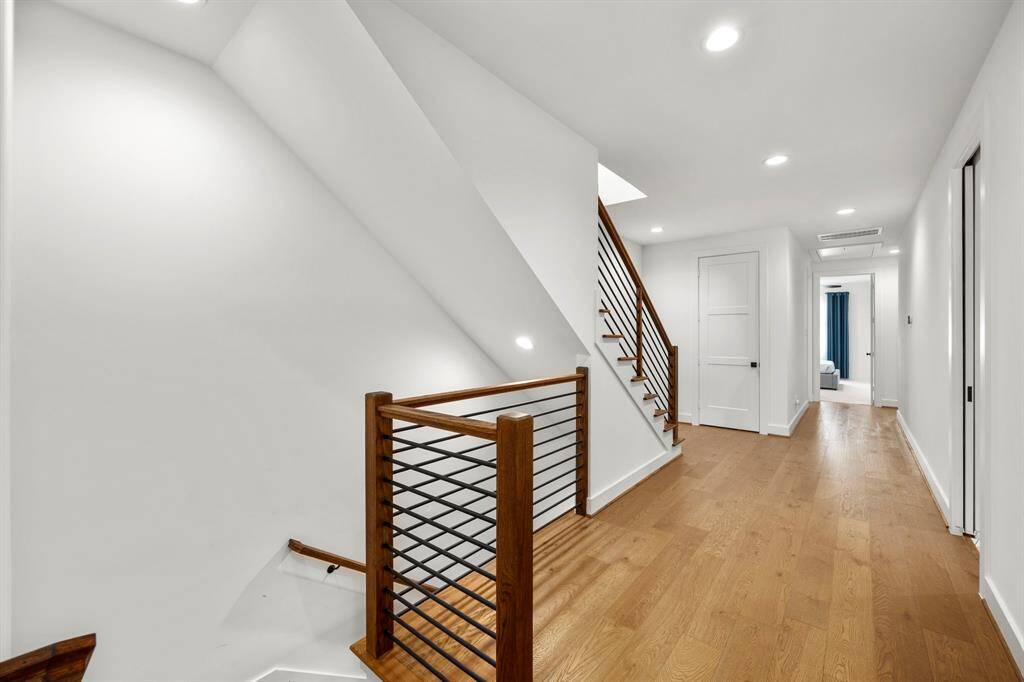 This view of the second-floor landing showcases the elegant staircase with modern wood and metal railings. The hallway features warm wood flooring and leads to additional rooms, offering an open and airy space enhanced by clean lines and recessed lighting. The layout seamlessly connects the upper floor with the rest of the home, creating a natural flow.