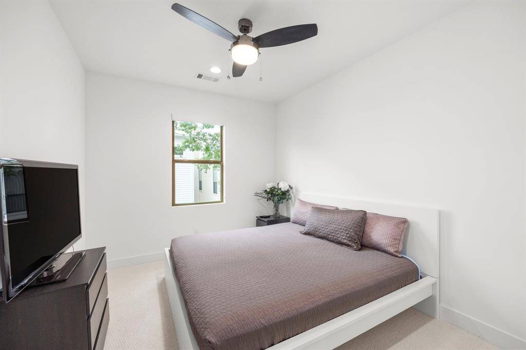 This secondary bedroom offers a spacious and serene retreat, featuring soft neutral tones, plush carpeting, and a ceiling fan for comfort. A large window provides natural light, enhancing the room's bright and airy feel.