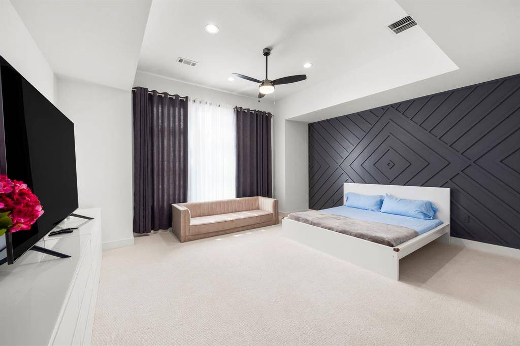 This view of the primary bedroom highlights a striking wood-paneled accent wall that adds texture and depth to the space. The recessed ceiling with modern lighting complements the clean, minimalist design, creating a sophisticated and tranquil retreat.