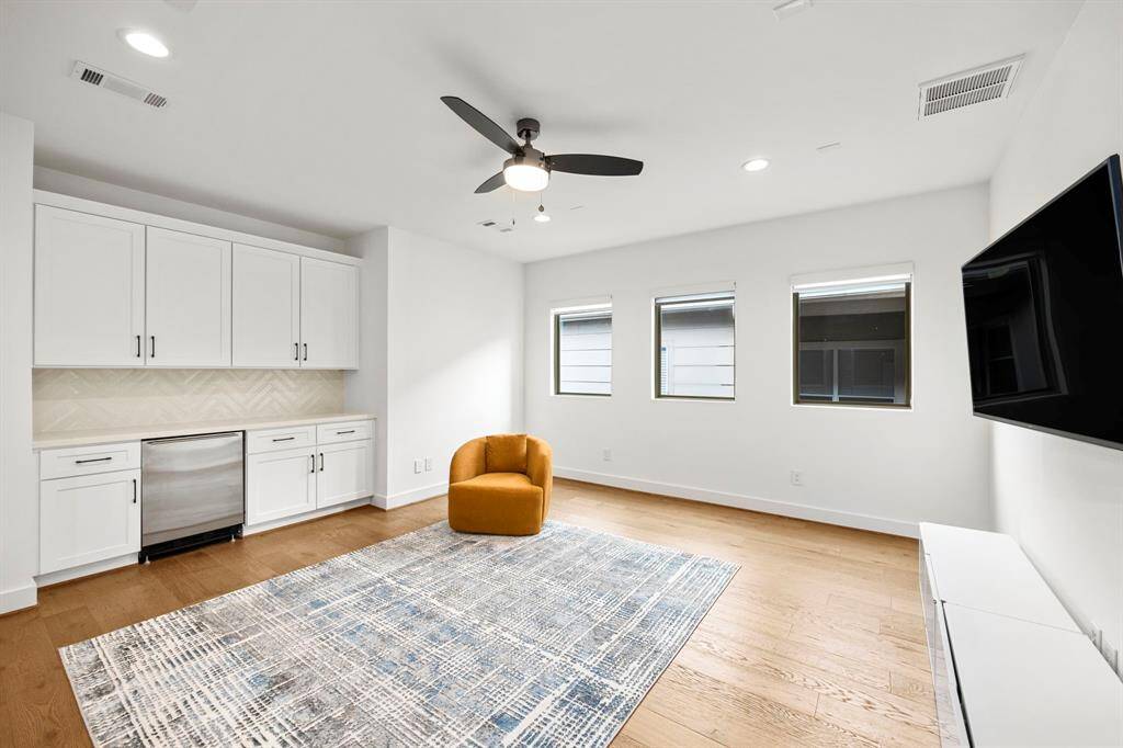 The spacious flex room offers versatility and features a built-in bar area with cabinetry and a mini fridge. The large windows provide natural light, while the open layout makes this room ideal for entertainment or a home office setup. The bar area is complemented by a stylish backsplash, adding a functional and attractive design element.