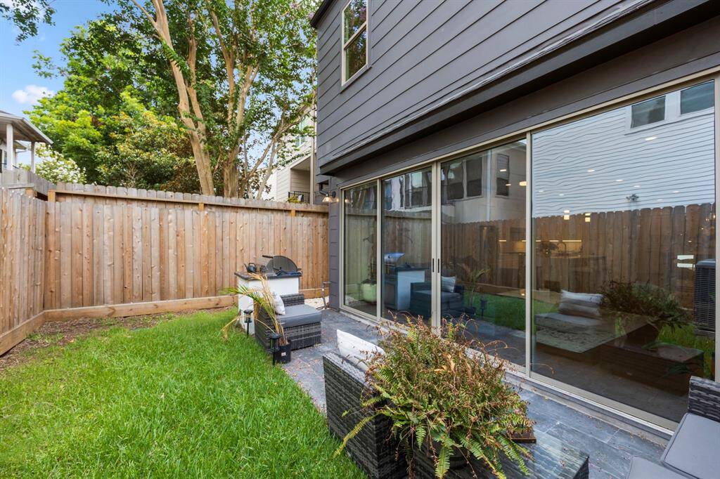 Additional view of the backyard highlights the spacious patio area and lush green space, perfect for outdoor activities and entertaining. The privacy fence adds seclusion, while large sliding doors connect the interior living space seamlessly to the outdoors, enhancing the indoor-outdoor flow.