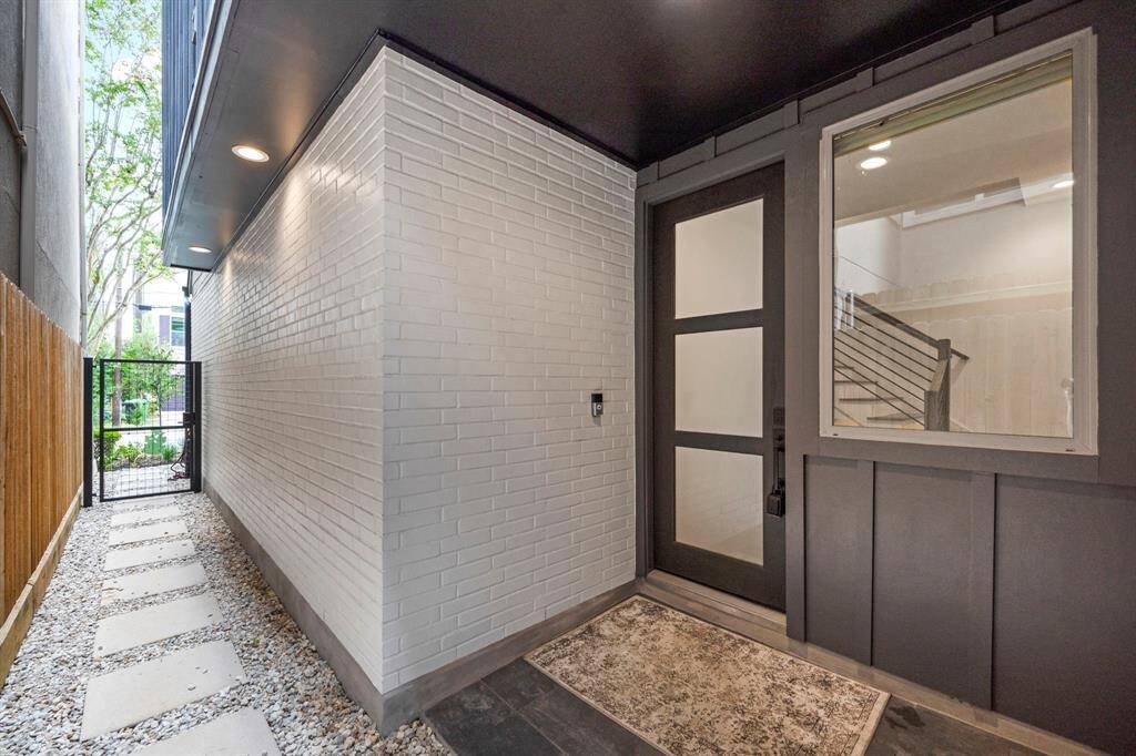 This inviting front entry view showcases a sleek modern door framed by clean white brick and a well-lit path leading to the street. The elegant walkway, with stepping stones set in gravel, offers a seamless transition between the privacy of the home and the vibrant neighborhood beyond.