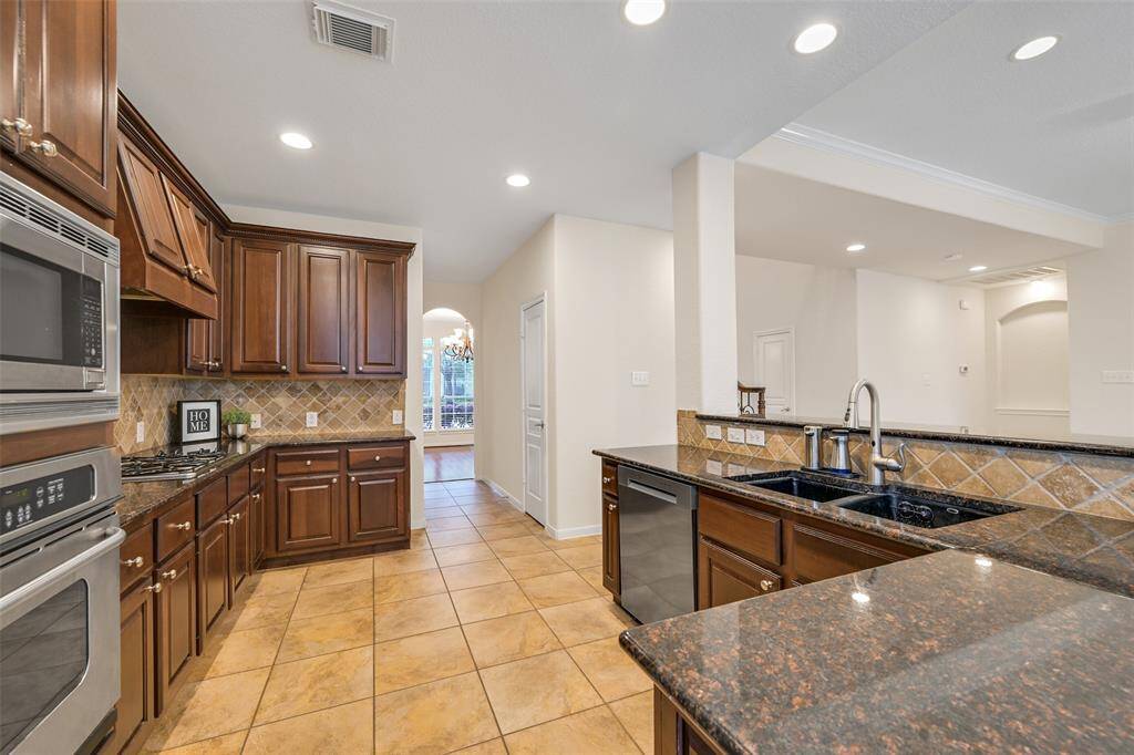 A wrap-around breakfast bar with granite countertops and ample seating space extends into this spacious kitchen with rich wood cabinetry, a diagonally laid tile backsplash, a gas cooktop, and double ovens—ideal for the home chef.