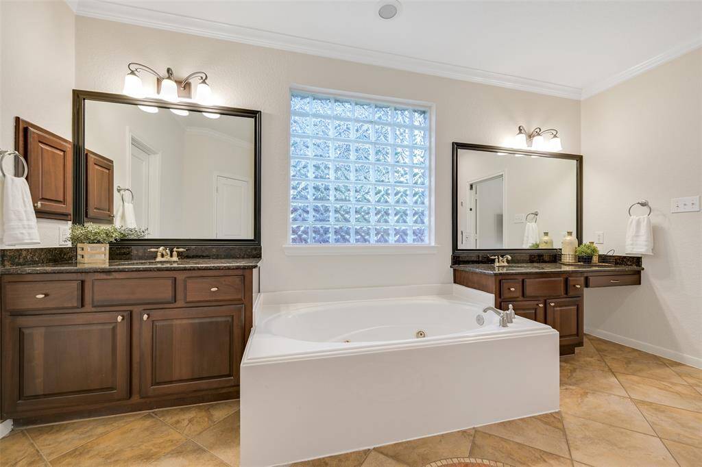 The spa-inspired en-suite bath features separate his & hers granite-topped vanities with richly stained cabinetry & framed mirrors, separated by a deep jetted soaking tub with a privacy glass window that fills the space with natural light while maintaining seclusion.