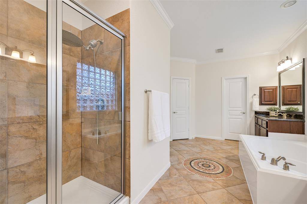 Opposite the dual granite vanities & a deep jetted soaking tub, note the and intricate tile accents on the floor and the large walk-in shower with a rainfall showerhead, a tile enclosure, and a glass door - all designed for a spa-like retreat.