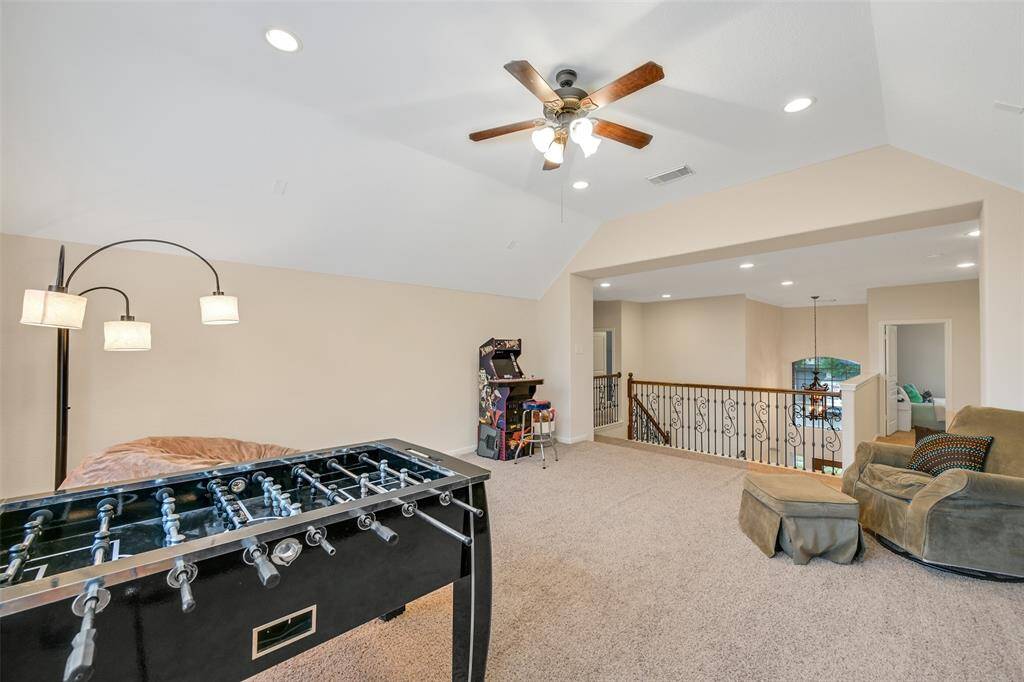 A split staircase with wrought iron balusters delivers you to this centrally located upstairs game room with plush carpet, a raised gambrel ceiling, and views into the foyer—perfect for entertaining, relaxing, or hosting game nights.