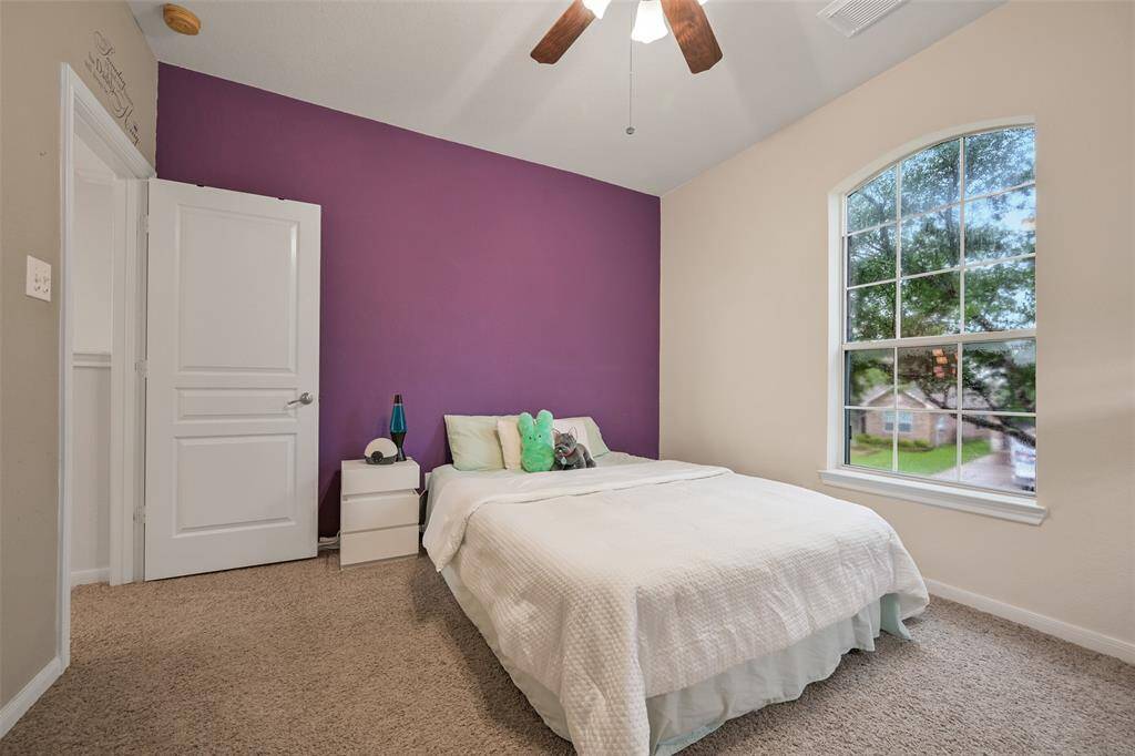 The first of four upstairs secondary bedrooms that are all on opposite corners of the game room features a lighted ceiling fan, a front-facing palladium arched window, a roomy walk-in closet, and a bold accent wall for a pop of personality.