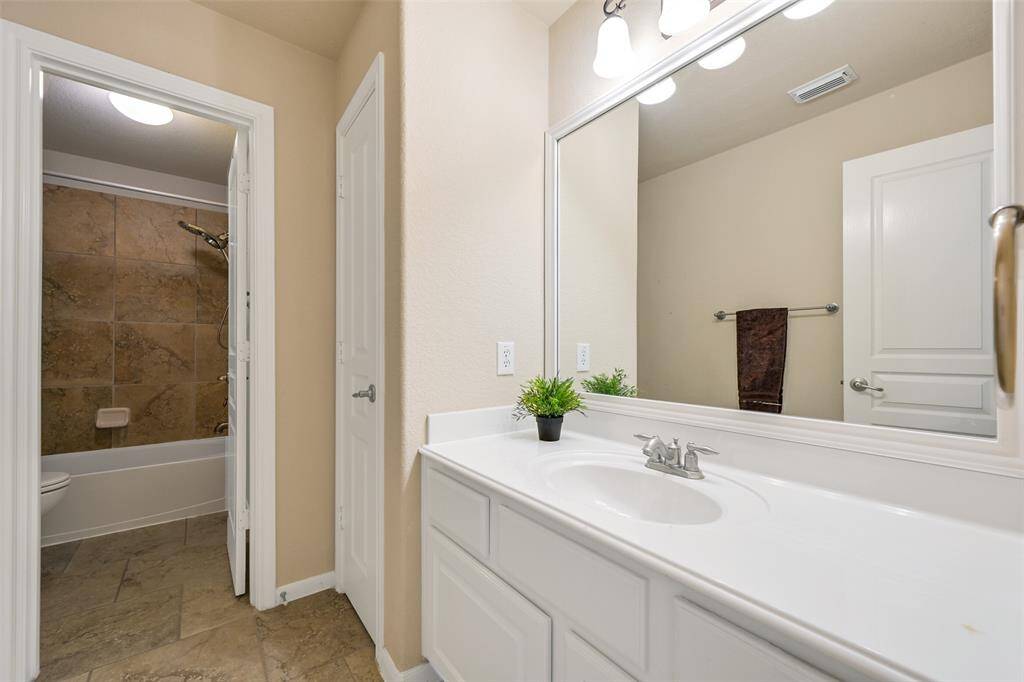 This full bathroom services the previous bedroom and the next bedroom, offering a large framed mirror, bright lighting, a cultured marble countertop with a basin sink, white cabinetry, and a separate shower/tub combo with a tile surround.