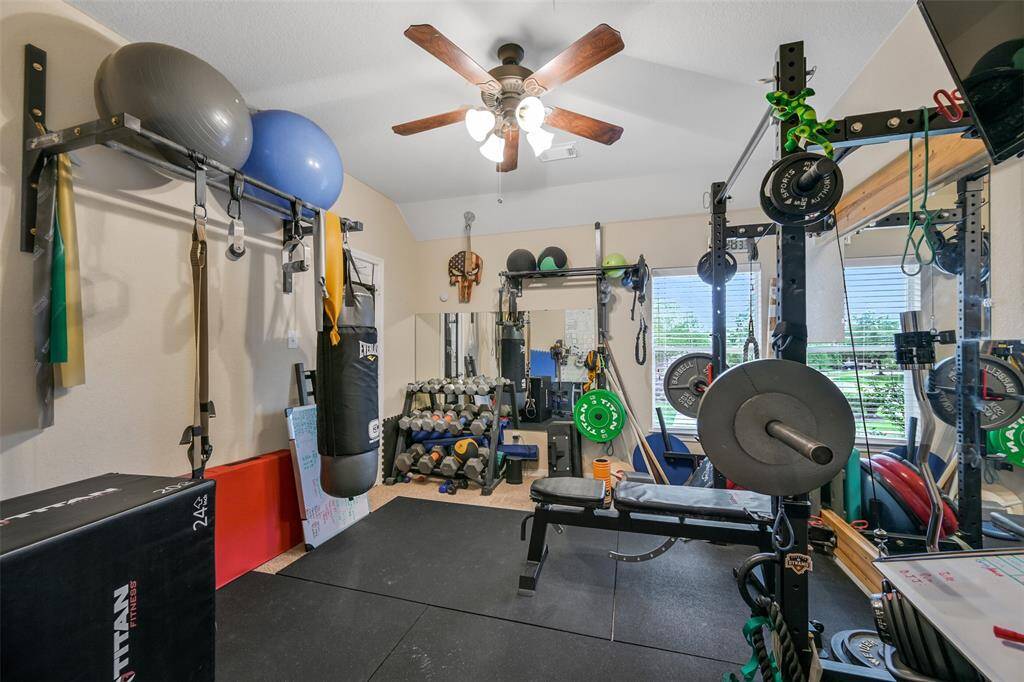 One of the spacious secondary bedrooms, currently utilized as a home gym, offers ample space, natural light from a front-facing window with 2-inch blinds, a lighted ceiling fan, a step-in closet, and versatility to suit your lifestyle needs.