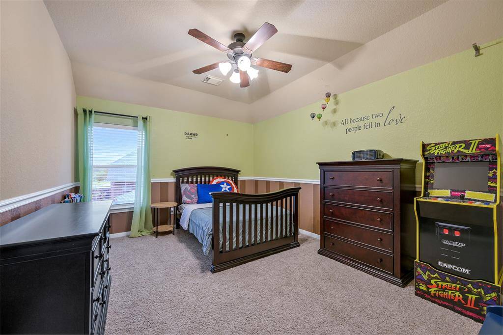 This secondary bedroom, located on the opposite side of the game room from the other upstairs bedrooms, offers privacy and charm with soft natural light, an elevated gambrel ceiling with a lighted ceiling fan, and a spacious layout perfect for guests or family.