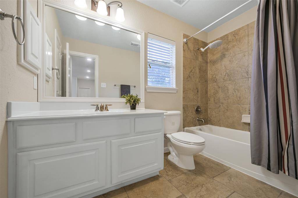This bathroom services the previous two bedrooms and it features a spacious cultured marble vanity with ample storage, a large framed mirror, and a tub/shower combo with oversized tile surround and a rainfall showerhead.