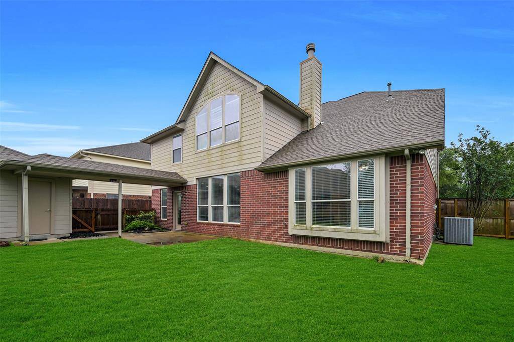 A full panel glass back door leads into this backyard that features a lush green lawn, a concrete patio space, and a detached garage connected by a covered breezeway—offering shade and convenient access to the home.