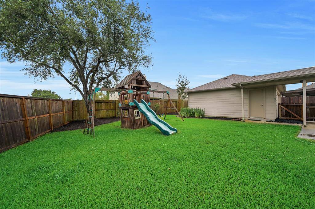 This fully fenced backyard offers generous green space, a mature shade tree with freshly mulched landscaping, and a wooden playset—perfect for outdoor fun and family enjoyment.