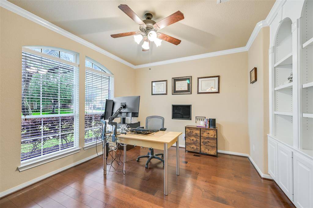 This private home office at the front of the home features French doors for privacy, engineered wood floors, elegant crown molding, a wall of custom built-in shelving, and a palladium arched front-facing window that fills the room with natural light.
