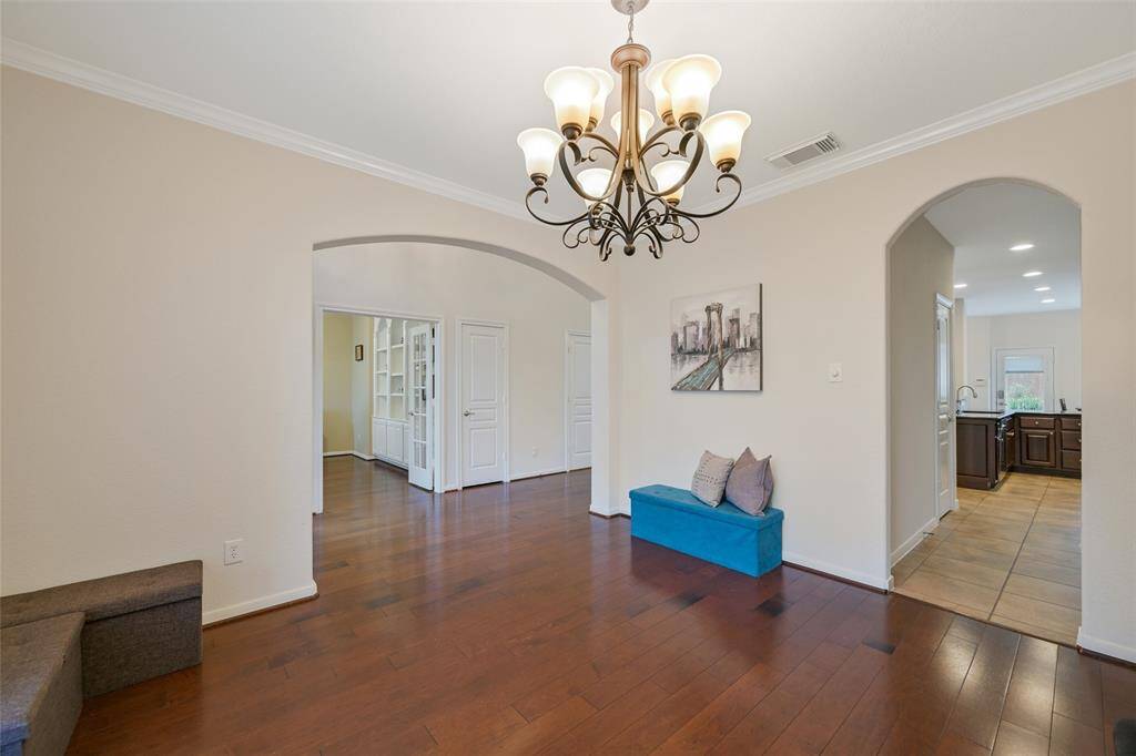 An elegant and inviting formal dining room is located just off of the foyer, featuring engineered wood floors, crown molding, a scrolled iron chandelier direct kitchen access, and a large front-facing window with arched transoms that fill the space with natural light.