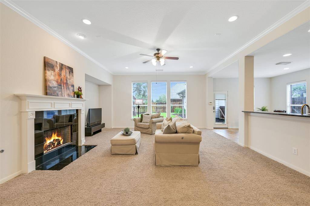 This inviting family room features a wall of windows that fill the space with natural light, a cozy gas fireplace with a sleek black granite tile surround, and an open layout that flows seamlessly into the kitchen and breakfast area—perfect for entertaining or everyday living.