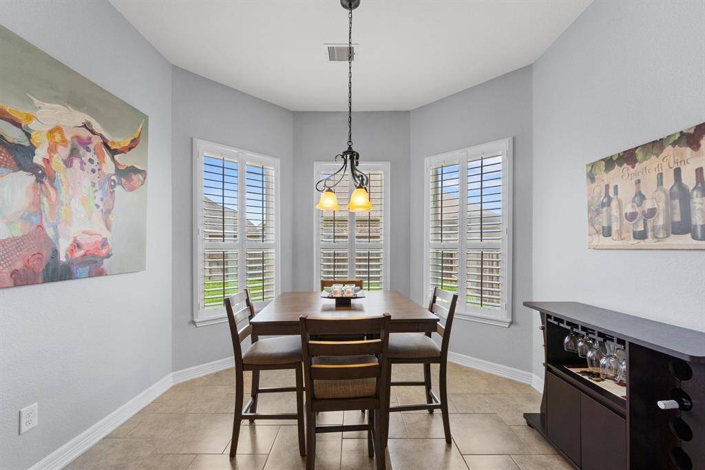 Charming breakfast area, complete with tile floors, pendant lighting, and beautiful views of the backyard are provided by several windows with shutter blinds.