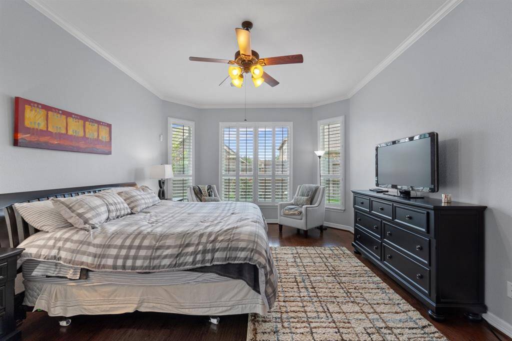 Unwind after a long day in this incredible Primary Bedroom! Featuring lots of natural light, wood floors, windows with shutters, crown molding details, and a ceiling fan.