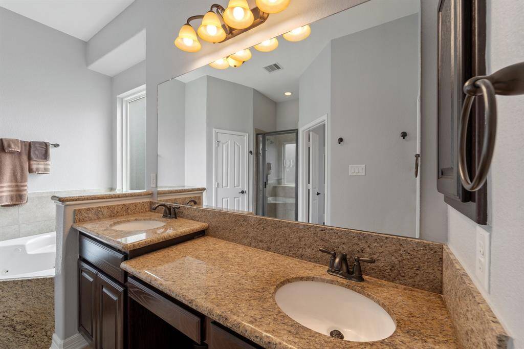 This bathroom is complete with a large mirror, double sinks, granite countertops and backsplash, and a vanity area.