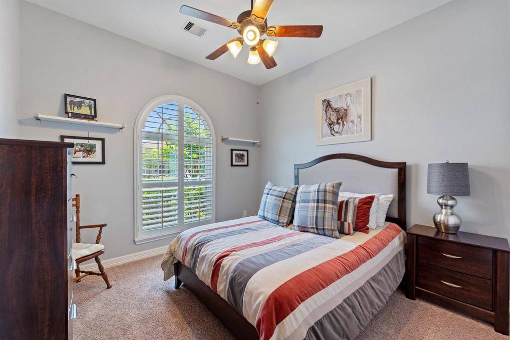 Secondary bedroom with carpet floors, a ceiling fan, and windows with shutters.