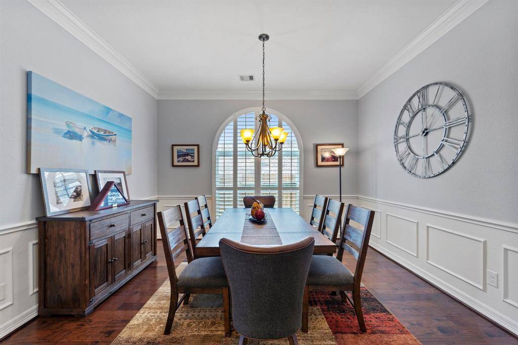 Spacious dining room with dark stained wood floors, pendant lighting, crown molding, and windows with shutters.