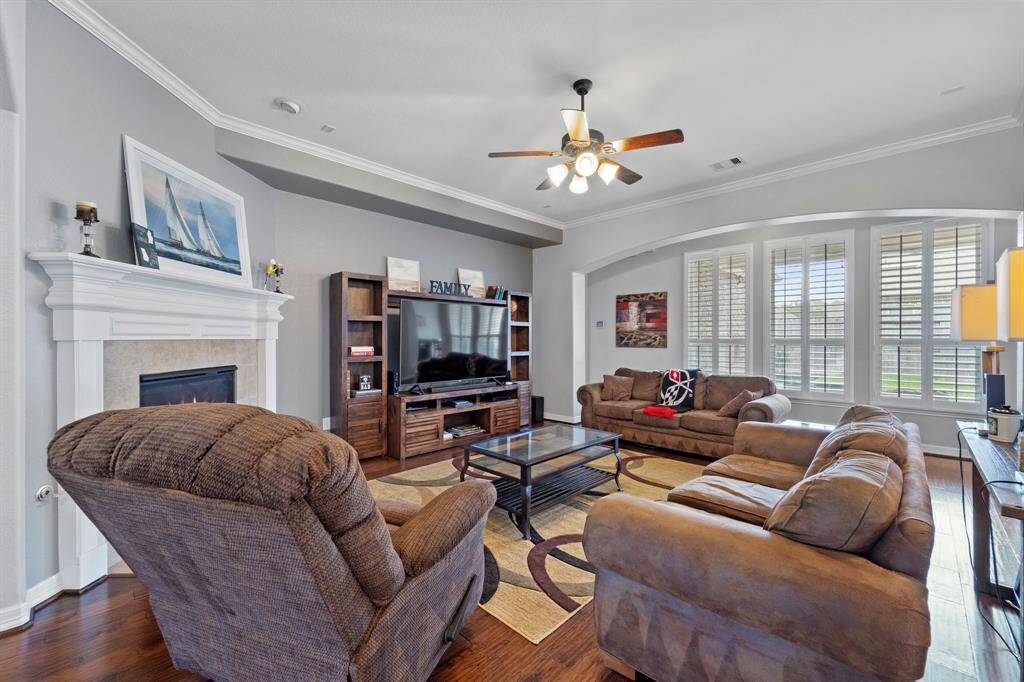 This stunning living room features crown molding details, a ceiling fan, wood floors, and great views of your backyard.