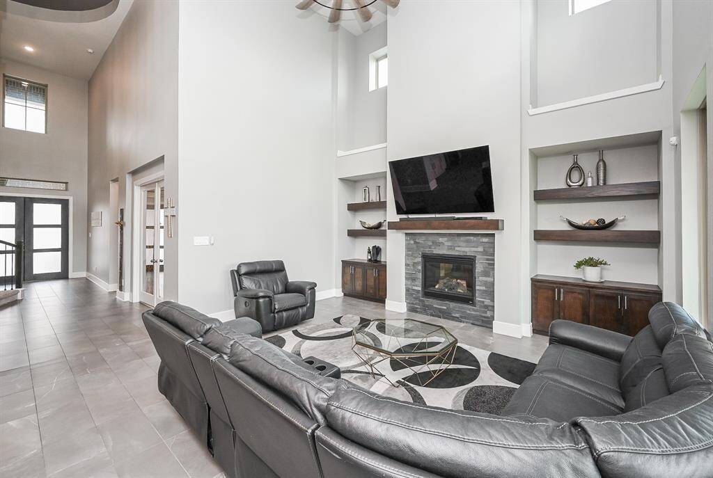 Delicate recessed ceiling lighting adds to the sublime combination of natural light from fun square high windows, embracing neutral tones on walls and lush tile flooring. Generous shelving on either side of the stone encased gas log fireplace, will house your favorite reading material and honored display pieces. Imagine this incredible space filled with family and friends for holiday (or any day) entertaining.