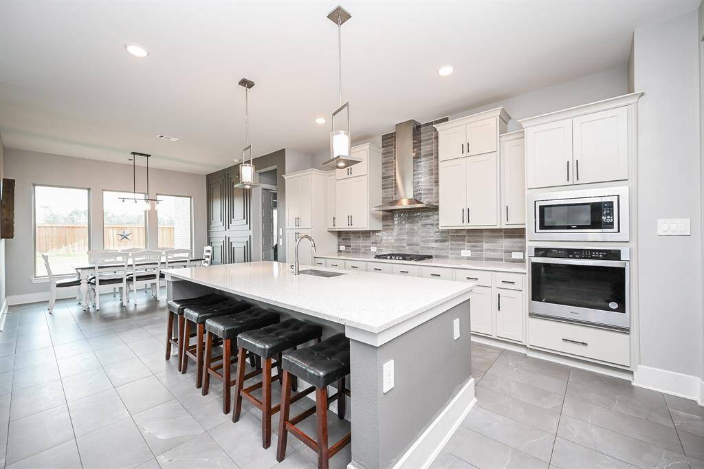Not only is this kitchen visually exciting and, at the same time, relaxing, it is also chock full of cabinetry up and down, with soft toned tile backsplash and an oversized island, with plenty of clever knee room for a host of comfy stools; and a large breakfast nook, left.