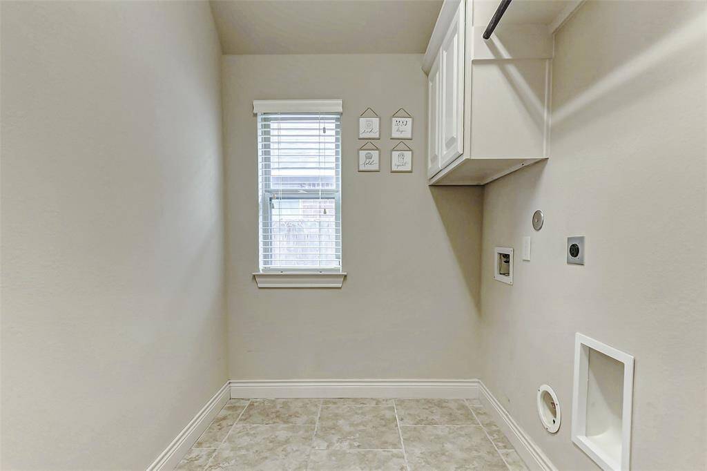 This utility room features a window for natural light, tiled flooring, and hookups for a washer and dryer. Wall-mounted cabinets offer additional storage space for all your cleaning needs.