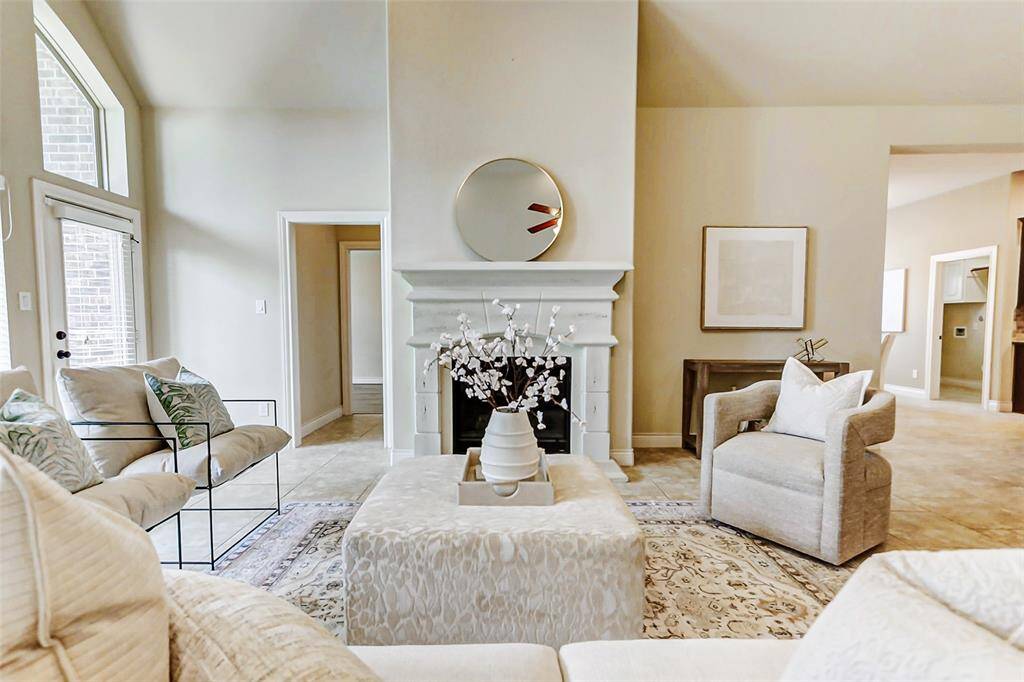 This bright living room features high ceilings, a cozy fireplace, and large windows for ample natural light. The neutral tones and elegant decor create a welcoming and stylish atmosphere, perfect for relaxation and entertaining.