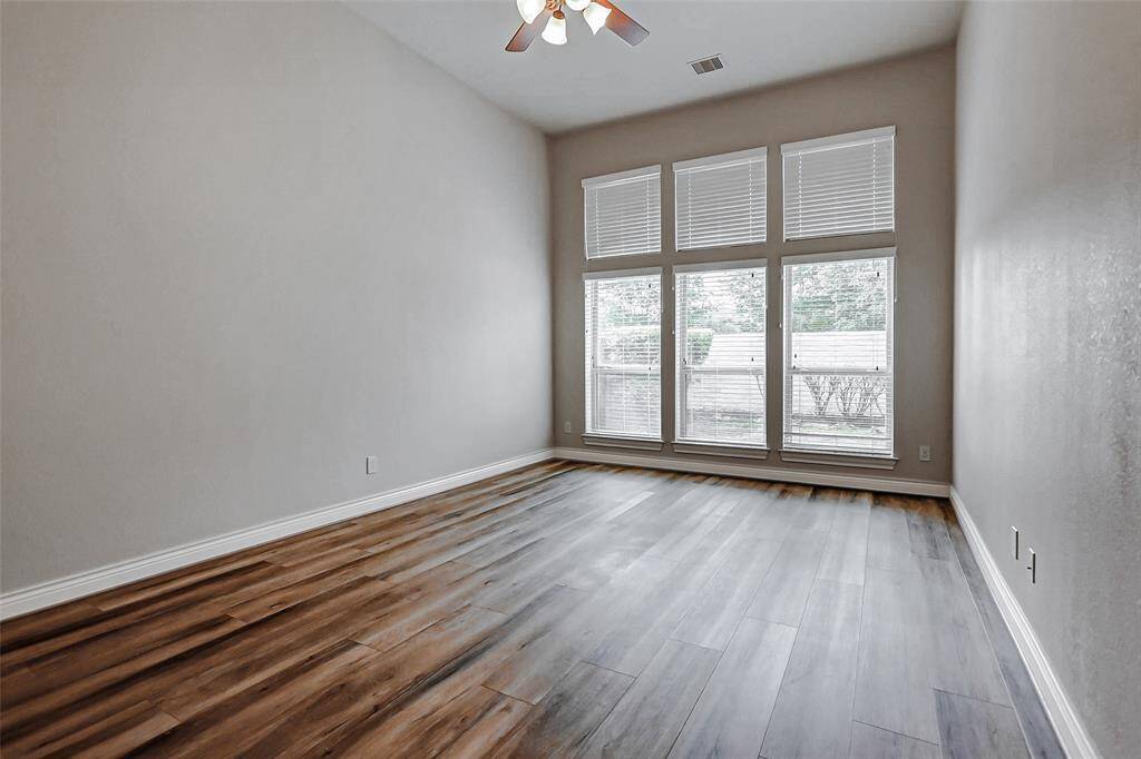 This spacious primary bedroom features 12' ceilings, ceiling fan, wood flooring and a wall of windows bringing in natural light throughout the day.