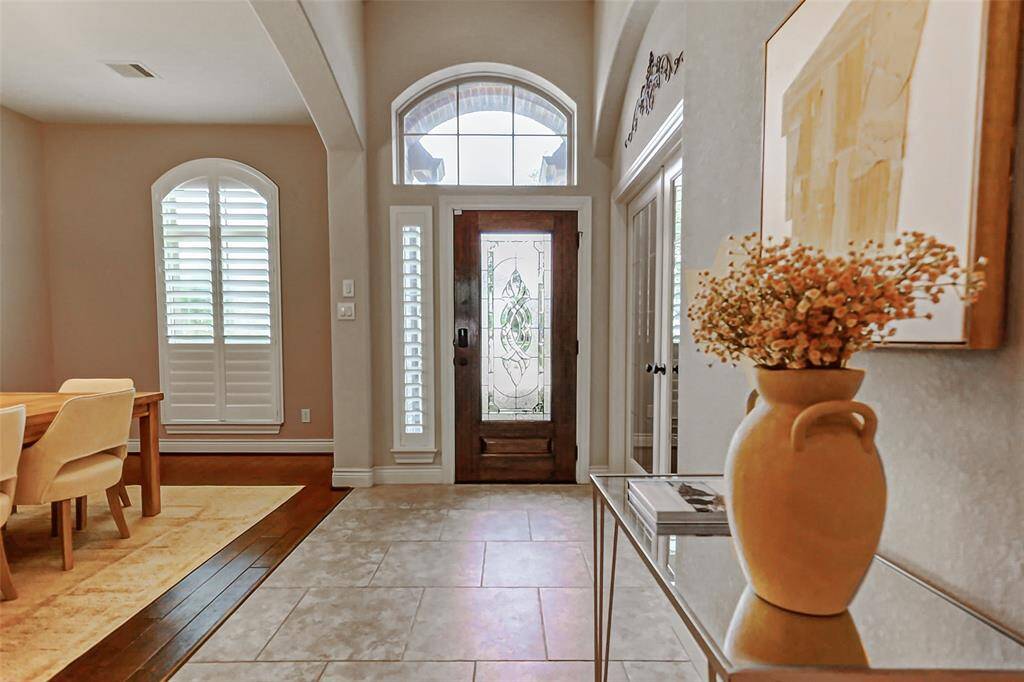 This entrance is welcoming and features a decorative glass front door, and abundant natural light. The adjacent dining area features hardwood floors and Plantation shutters, adding warmth and sophistication to the space.