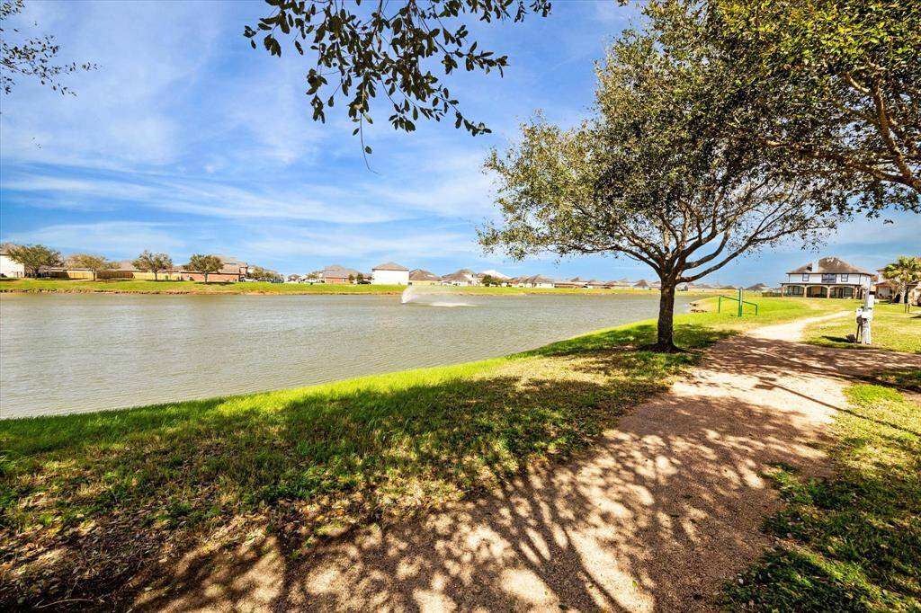 A serene neighborhood setting with a winding path along a tranquil lake, shaded by trees