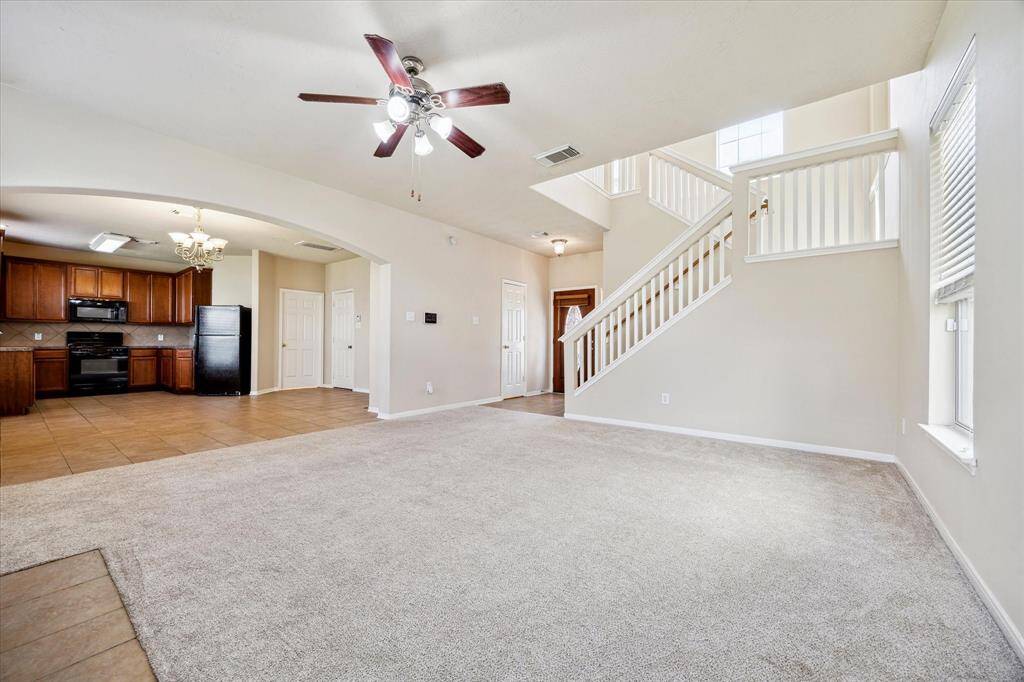 This spacious living area features an open floor plan with carpeted flooring, a ceiling fan, and plenty of natural light
