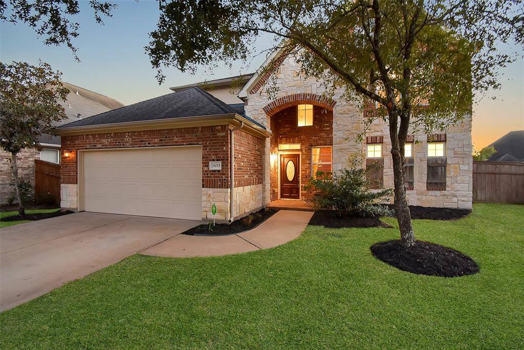 This charming home features a brick and stone exterior with a welcoming arched entryway. The well-maintained front yard includes lush green grass and mature trees. A spacious driveway leads to a two-car garage, offering ample parking and storage.