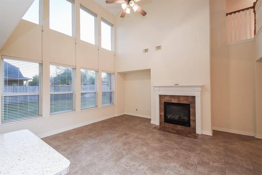Bright living room with high ceilings, large windows, and a ceiling fan plus a cozy fireplace