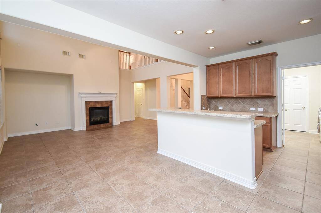 The kitchen with ample cabinetry and a breakfast bar. The room is bright with recessed lighting and has a view of an upstairs landing.