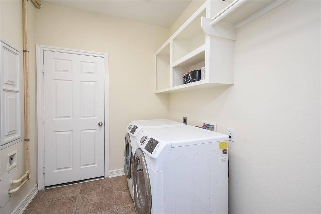 A clean and functional laundry room with a washer and dryer, & overhead shelves for storage